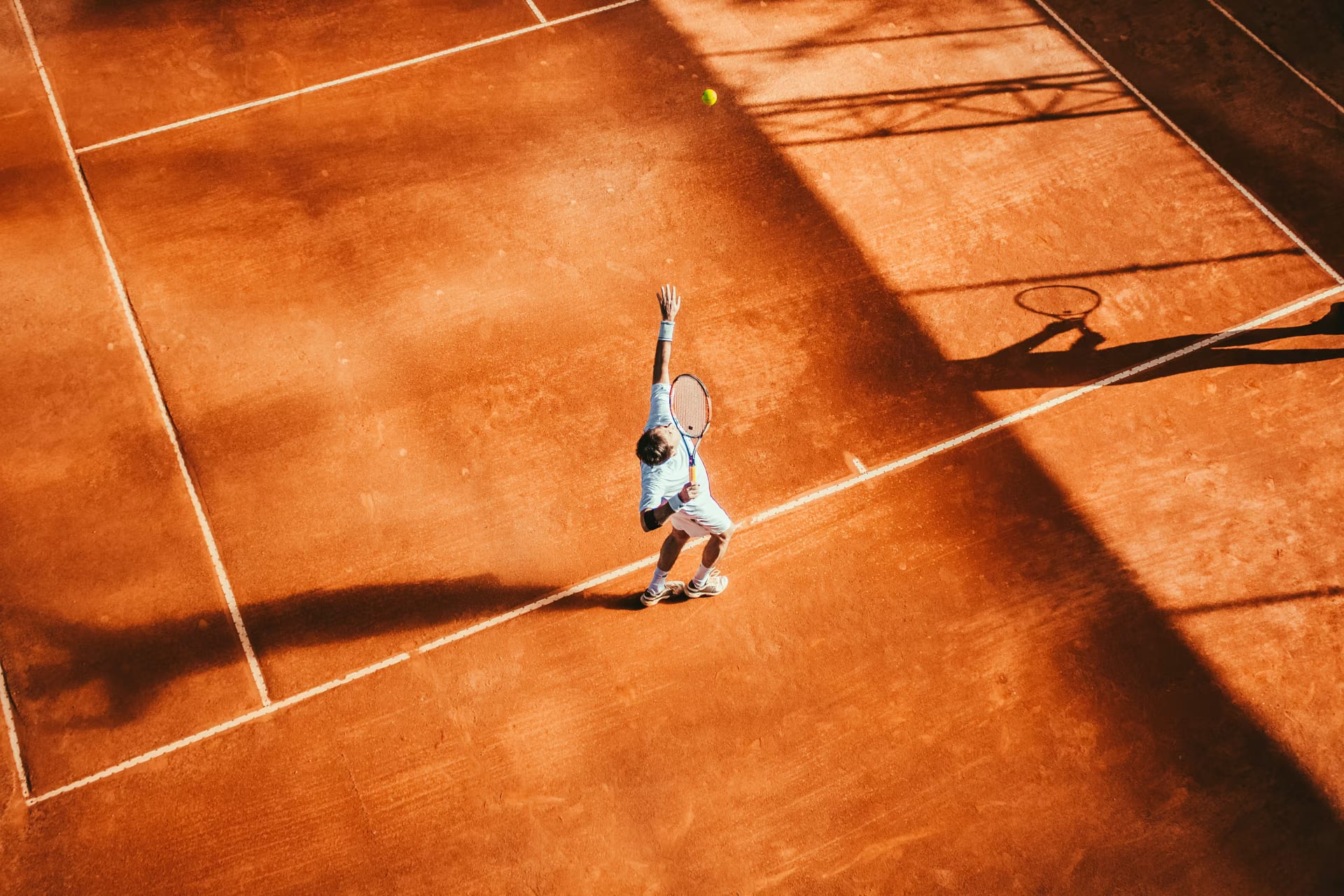 A tennis player serving on an orange clay court, seen from above